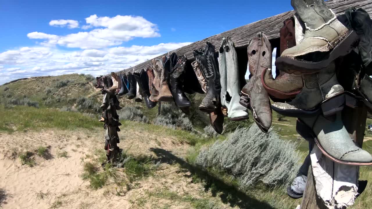 botas de vaquero colgando de un poste de madera en el campo en un día soleado