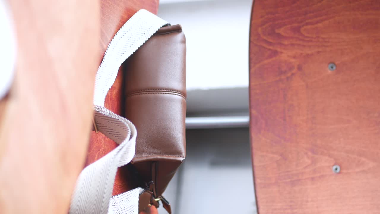 Close-up of a brown leather bag with a white strap next to a wooden surface