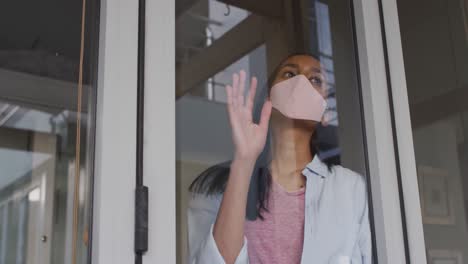 mixed race woman wearing mask at home looking through window