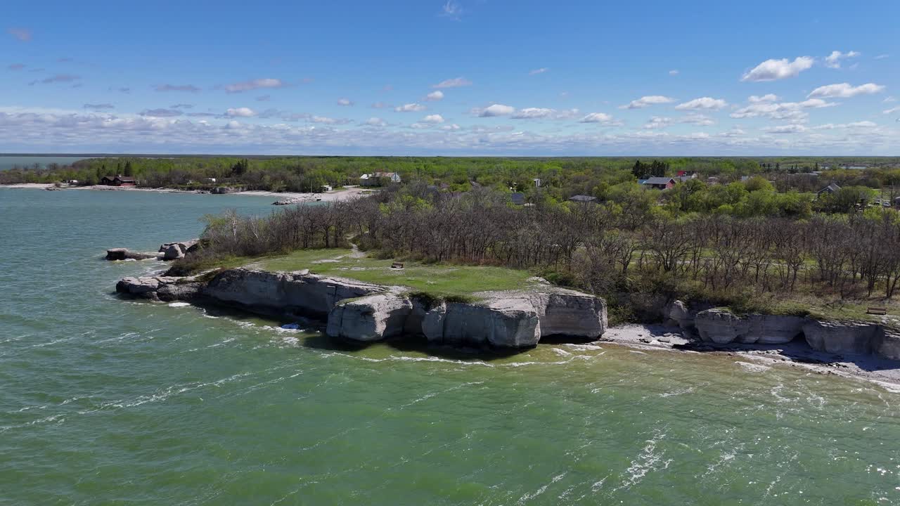 Flycam bay vòng sang trái trong khi hạ xuống và di chuyển về phía những vách đá vôi tại Steep Rock Manitoba, hiện ra bờ hồ, cây cối và mặt nước xanh của hồ Manitoba vào một ngày hè.