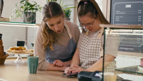 Mädchen-Mit-Down-Syndrom-Surft-Zusammen-Mit-Ihrer-Arbeitskollegin-Im-Café-Am-Telefon-Und-Unterhält-Sich