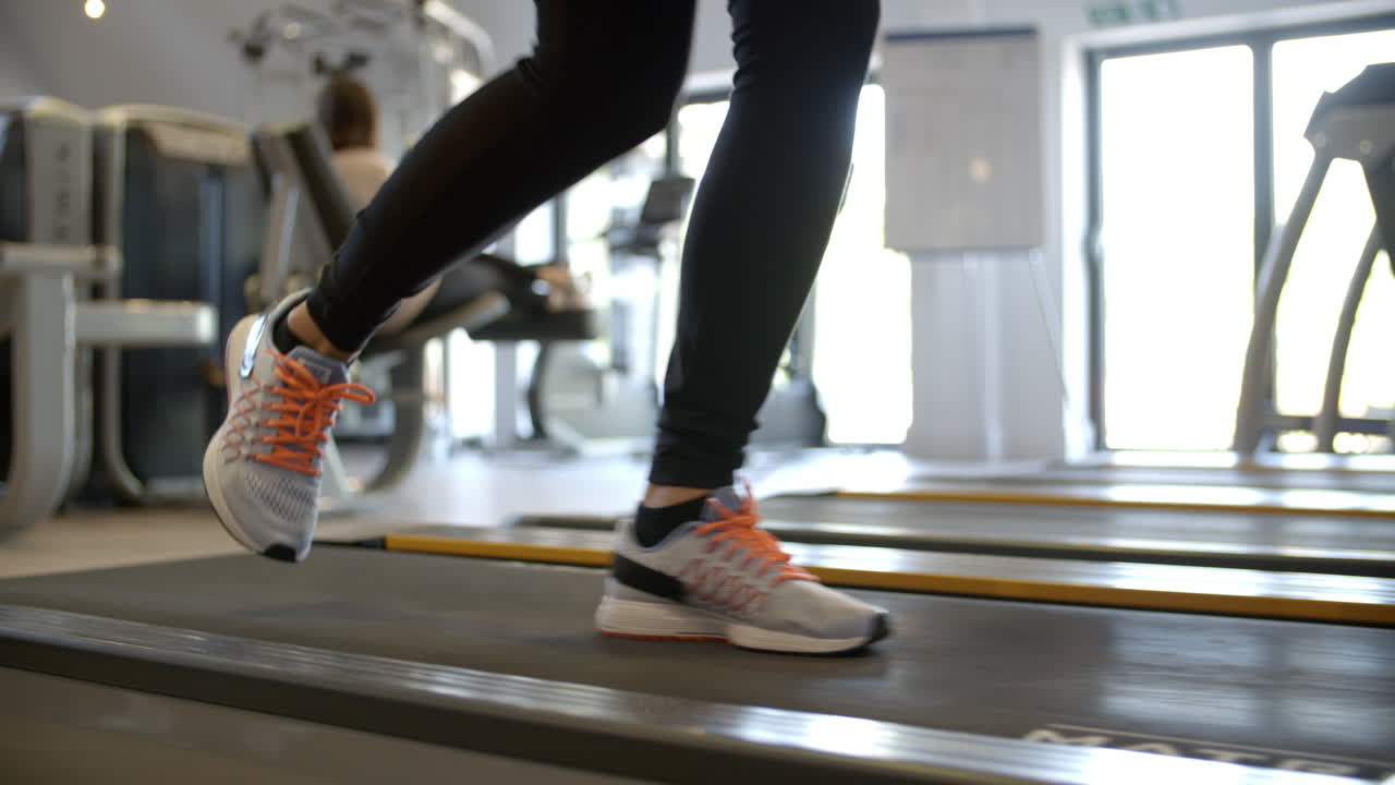 Woman exercising on running machine at a gym, low section