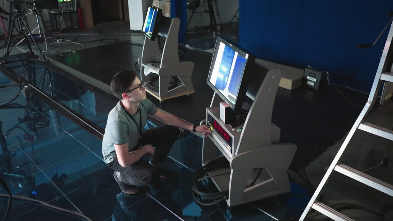 Man crouching and adjusting digital timer and monitor settings in modern production studio, focused on high-tech equipment, screen displaying data, professional editing setup in background