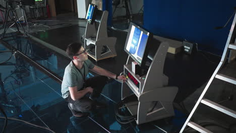 man crouching and adjusting digital timer and monitor settings in modern production studio, focused on high-tech equipment, screen displaying data, professional editing setup in background