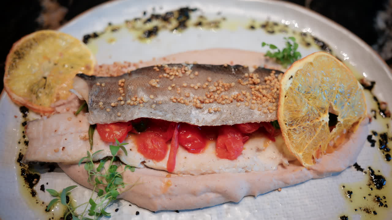 Close up of a beautifully plated fish fillet with sauce, lemon slice, and herbs