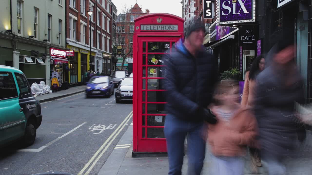 Time lapse of Red telephone box in London. United Kingdom. Peolple passing by a traditional telephone kiosk on sidewalk. Cars crossing the street on left side