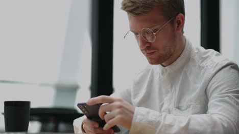 adult businessman texting on smartphone while sitting by laptop