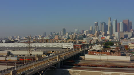 Los-Angeles-River-bridge-with-Power-lines-leading-into-Downtown-LA-Skyscraper-Skyline,-Scenic-Aerial-backwards-revealing-establishing-shot