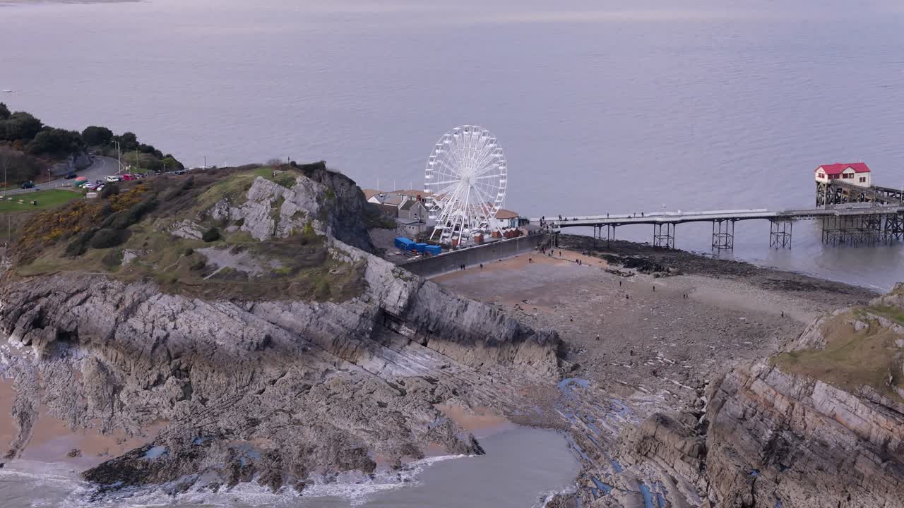 Aerial approach to the Ferris wheel at Mumbles Pier, slow rotation against the scenic coastal sky