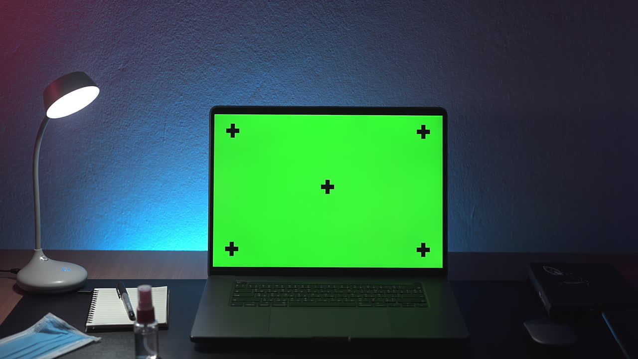 Mock-up di computer portatile con schermo verde, mascherina e disinfettante sulla scrivania in una stanza notturna