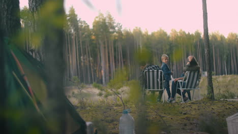 picnic of family at forest man and woman are sitting in armchairs and relaxing little children are playing near at nature camping in reserve