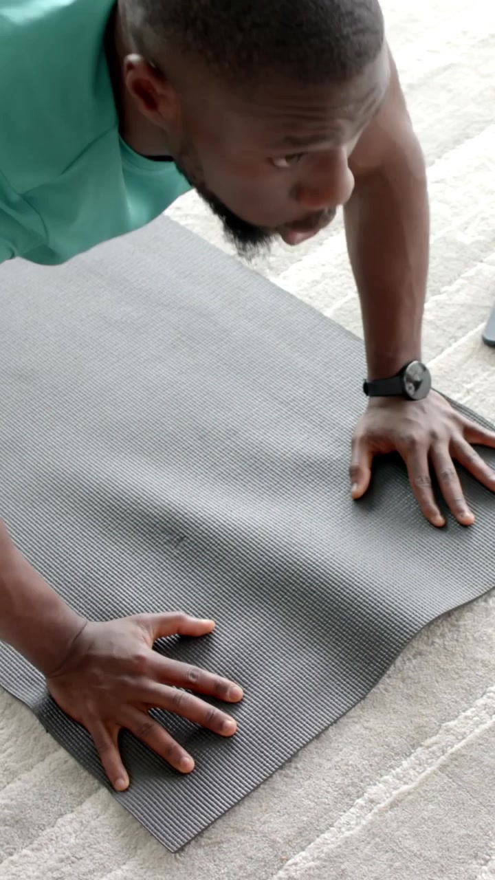 Vertical video: African American man training pushups placing hands on mat at home checking phone