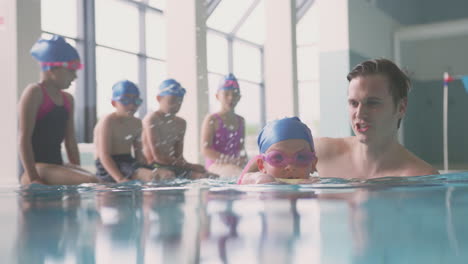 male swimming coach giving girl holding float lesson in pool