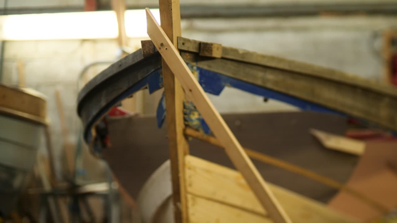 A close-up of a wooden boat’s bow in a workshop, showing new planks and reinforcements