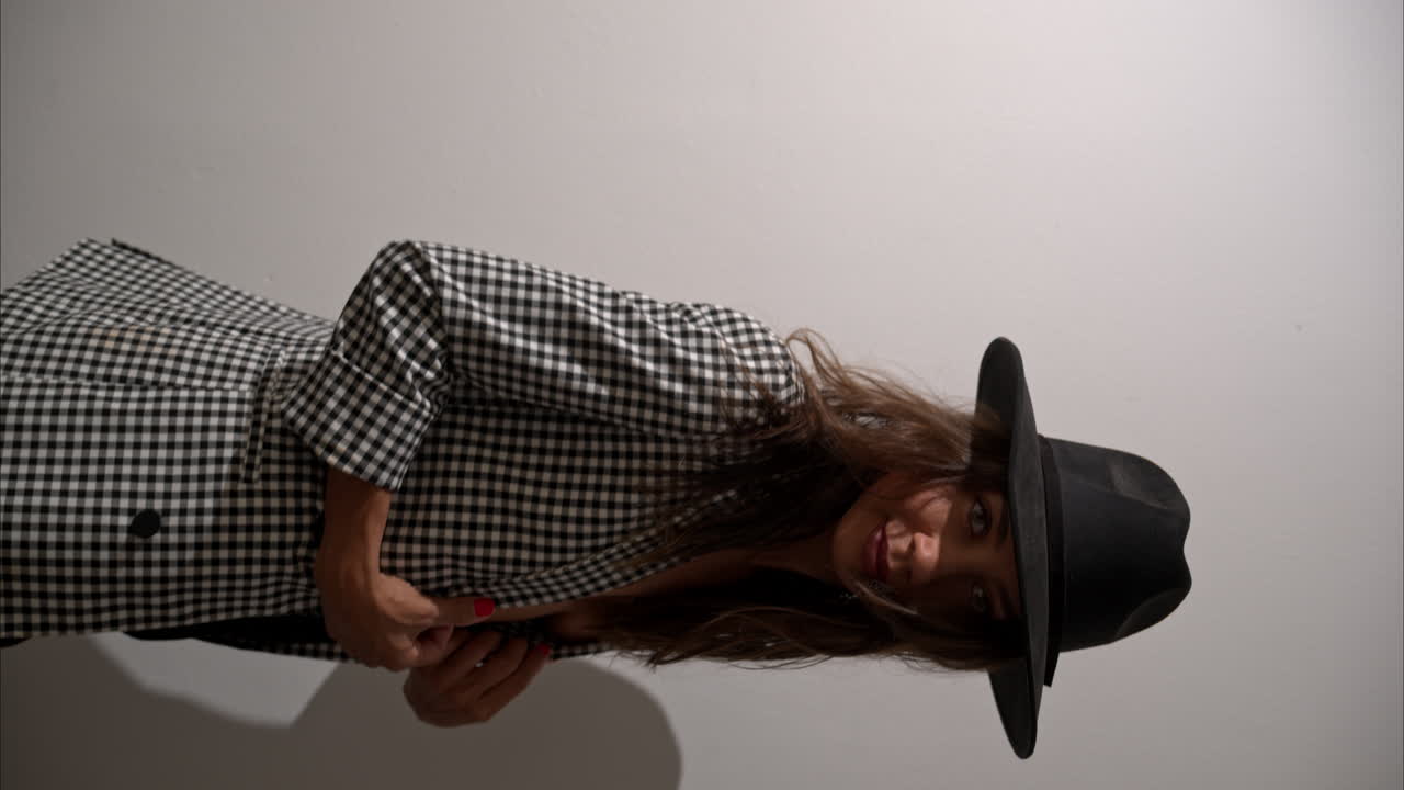 вертикальное замедленное движение сексуальной латиноамериканской женщины-модели в куртке и черной шляпе, поворачивающейся и позирующей.