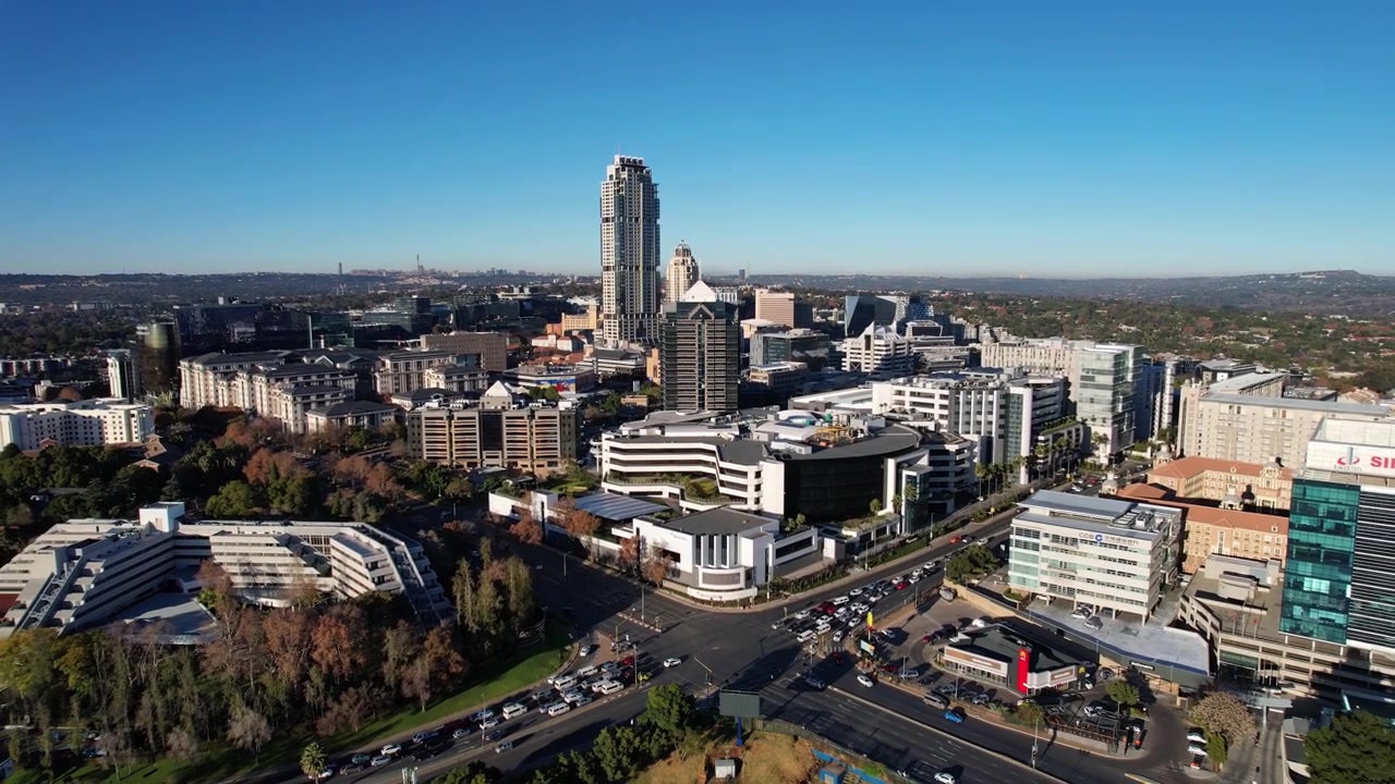 Sandtonin siluetti paljastuu hitaasti tässä ainutlaatuisessa ilmakuvassa, korostaen sen ainutlaatuista siluettia ja rakennuksia. Johannesburgin siluetti näkyy myös etäällä antaen kontekstia videolle.