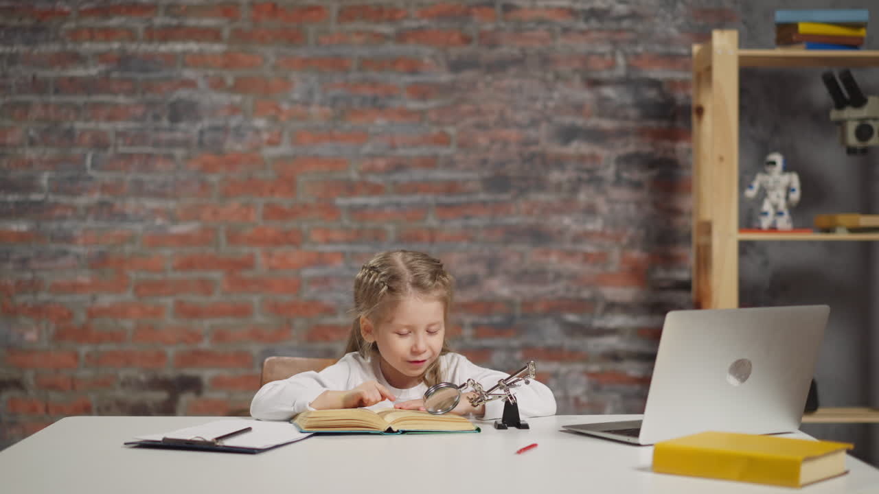 Little girl reads book with magnifier glass at large table