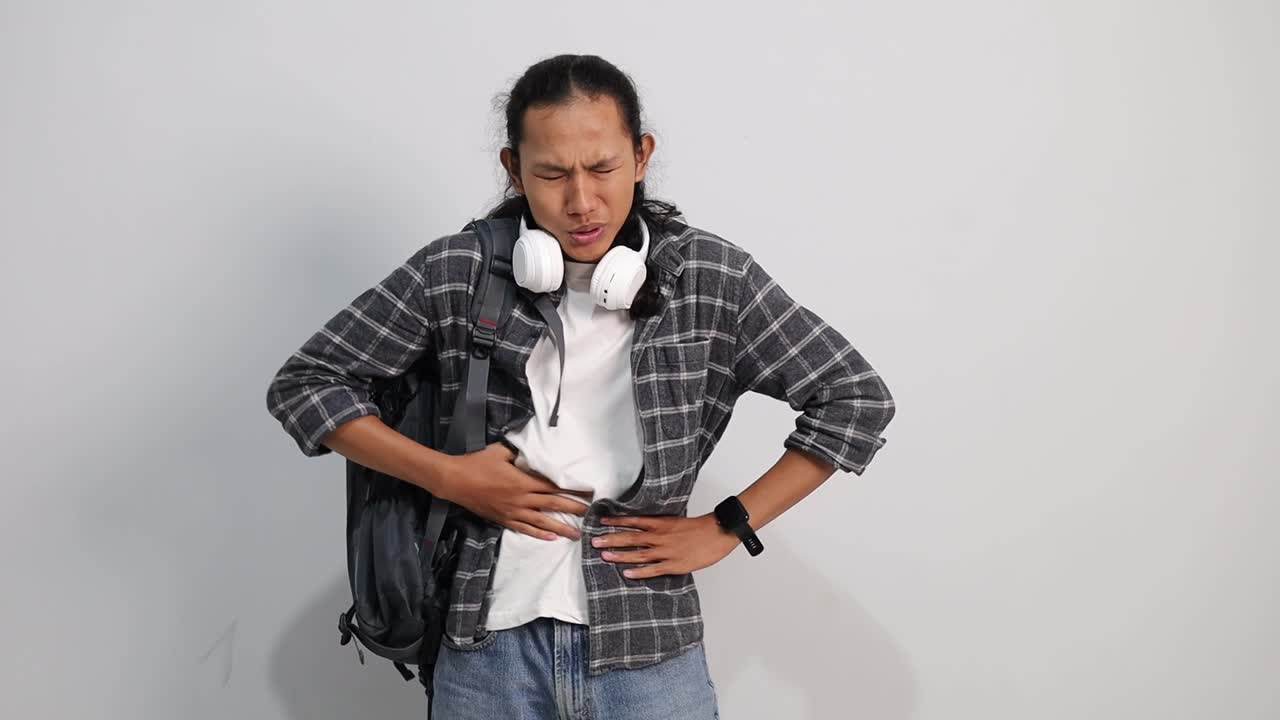 Young Asian college student touching his stomach isolated on white backgroun. Abdominal pain or ache concept