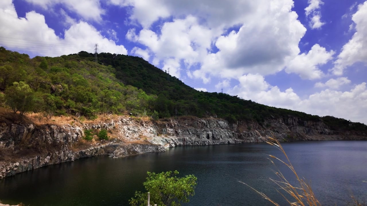 I visitatori si godono una giornata luminosa a Vung Tau, Vietnam, mentre nuvole soffici fluttuano sul lago. Alberi verdi costeggiano l'acqua, mentre la strada offre un facile accesso alla natura