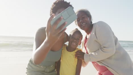 Happy-african-american-grandmother,-mother-and-daughter-taking-selfie-at-beach,-in-slow-motion