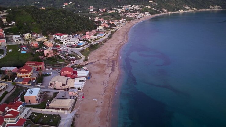 Voo de drone sobre praia de areia e hotéis de resort costeiro de Agios Georgios Pagon, Corfu, Grécia. Vista aérea da linha costeira do Mar Jônico e vila turística à beira-mar