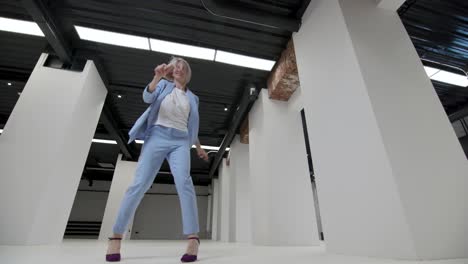 una mujer de negocios confiada de 30 años celebra ganando sin máscara. retrato despreocupado mujer de estilo urbano alegría mudarse a la sala de loft interior. cara alegre con movimientos tontos bucle. concepto exitoso baile divertido tiro ancho 4k