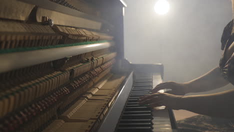 sexy woman surrounded by smoke playing dramatic music on vertical piano with open sound board