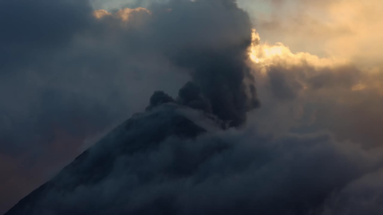 Volcano Fuego shrouded in cloud, emitting smoke and ash during dusk eruption, Guatamala