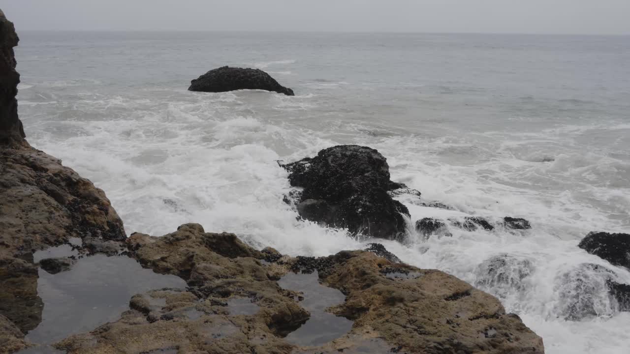 An intense close-up shot of powerful waves crashing onto the rugged rocks of Malibu's coastline, capturing the raw energy of the ocean