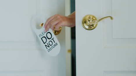 una mano femenina cuelga rápidamente un cartel de no molestar en la mano de una puerta