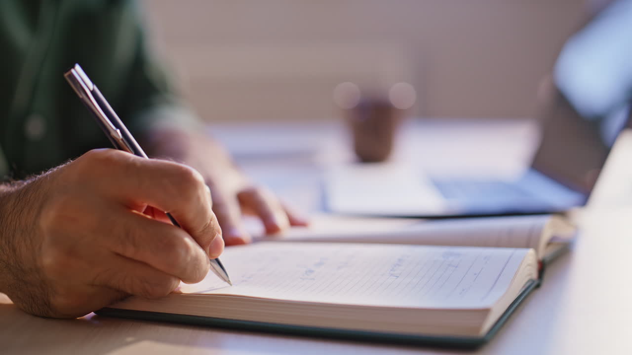 Serious student making notes in copybook studying online at workplace closeup