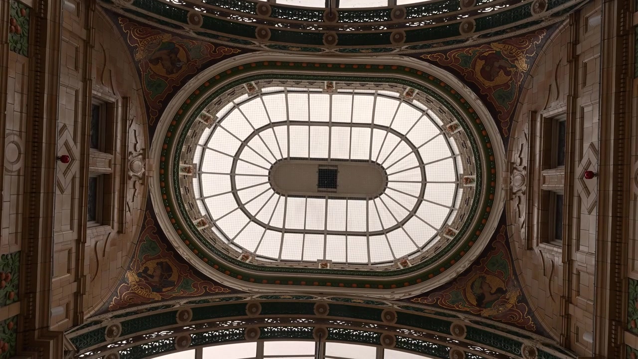 Il soffitto a cupola ovale in vetro decorato della galleria Victoria Quarter è incorniciato da architettura dipinta e intagliata in un'inquadratura statica dal basso verso l'alto.