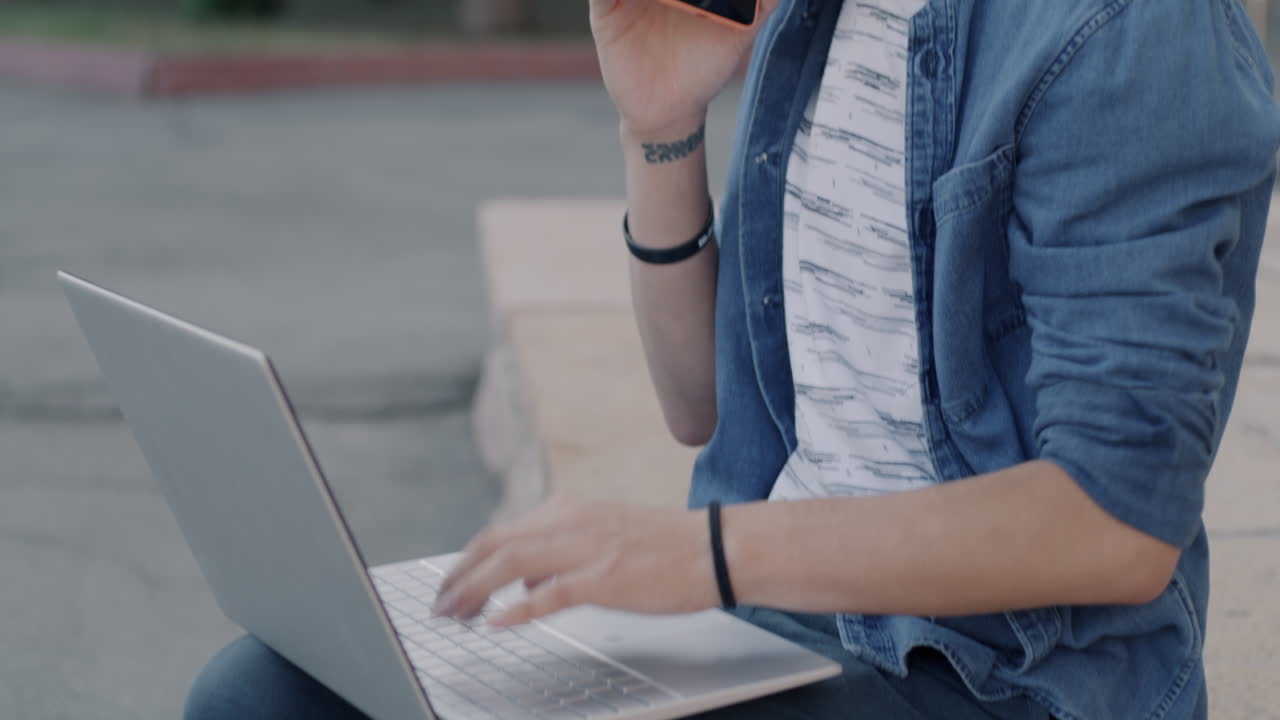 Teenage boy talking on phone and using laptop outdoors