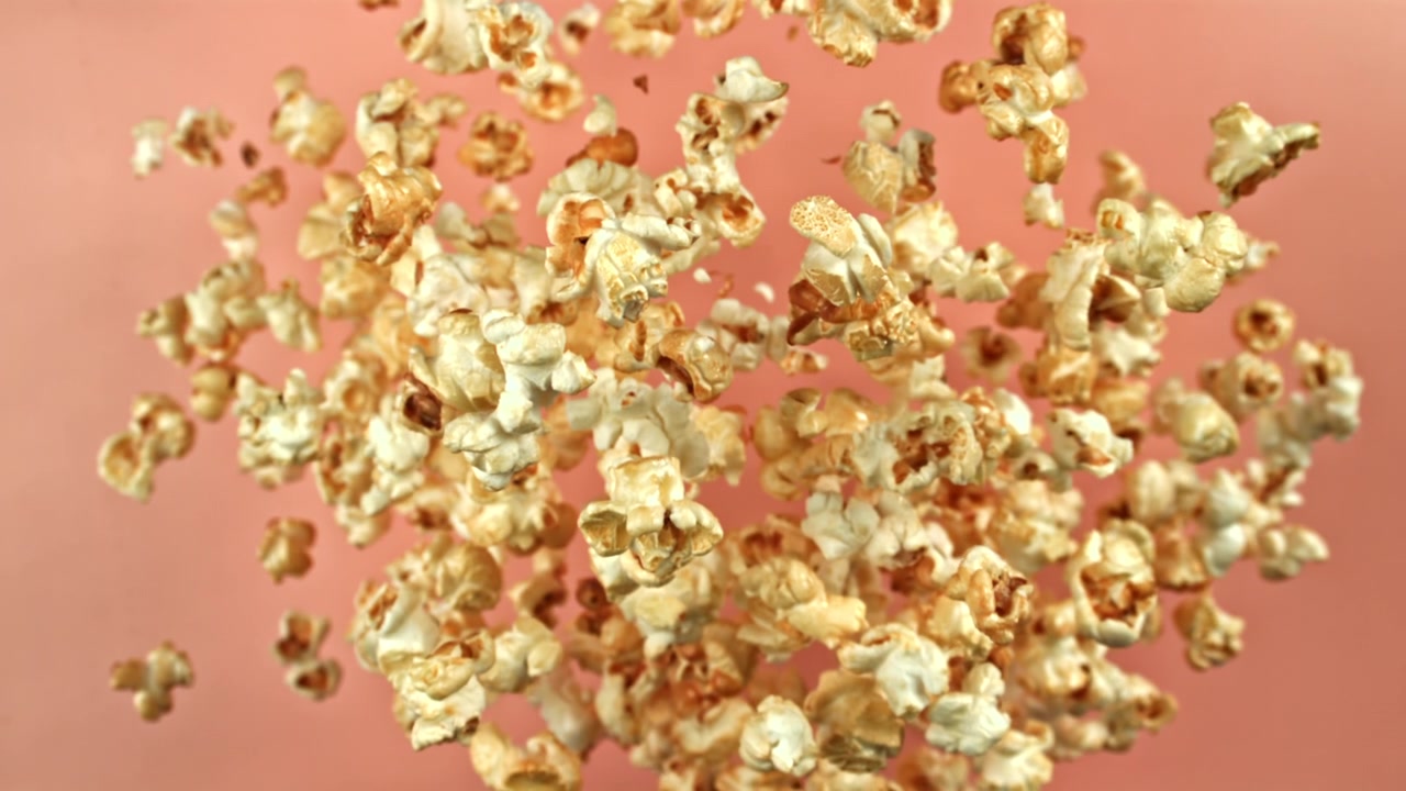 Popcorn Pieces Floating in Mid-Air Against a Pink Background