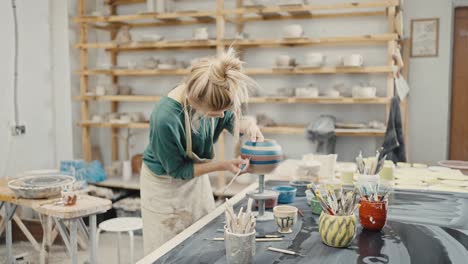 tracking shot of woman artist decoration handmade ceramic pot at pottery workshop, slow motion