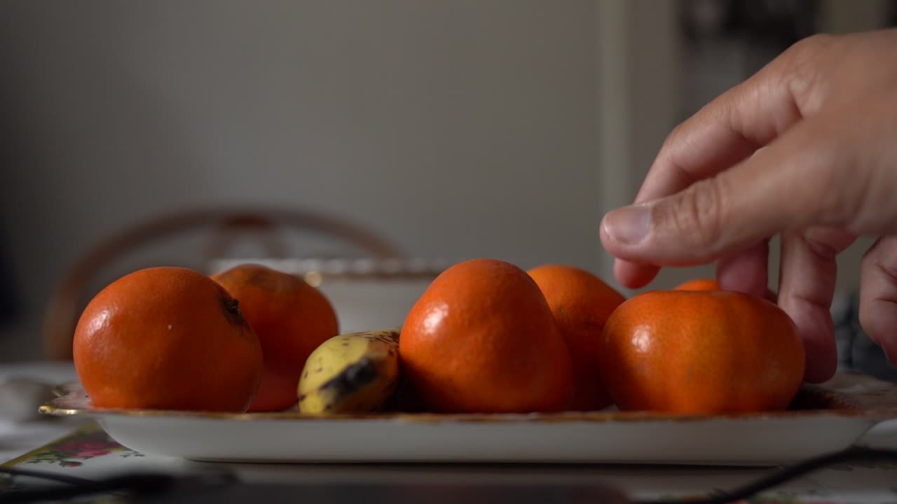 Mandehånd tager citrusfrugter fra en tallerken i slowmotion, tæt på.