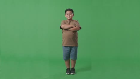 full body of asian boy crossed arms and warmly smiling on green screen background in the studio