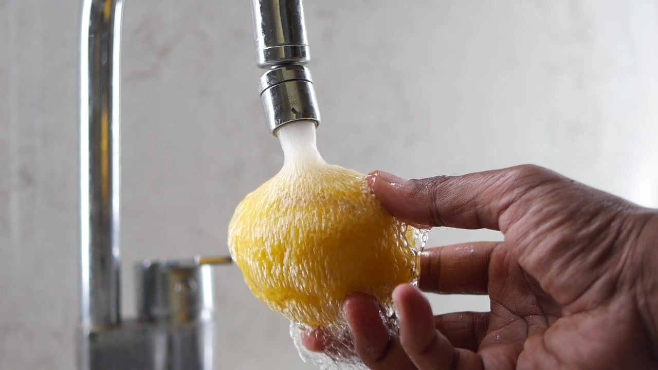 Mano lavando un limón fresco bajo el grifo de la cocina
