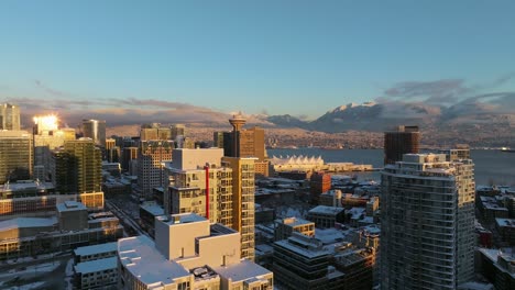 vancouver commercial buildings covered with snow during sunset with snow capped mountains in the backdrop