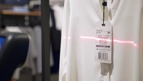 a close-up of a security tag on a white garment being scanned with a laser device in a retail clothing store, illustrating theft prevention measures in action