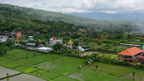 amusement-park-in-mountain-field-of-bali-with-airplane-and-ferris-wheel,-aerial