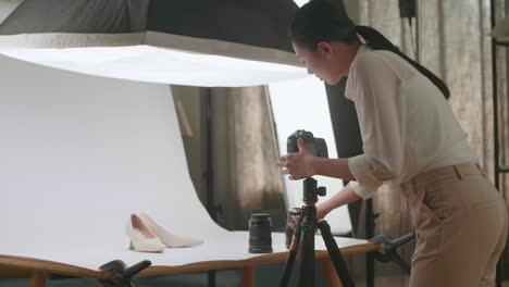 asian female photographer changing camera's lens while taking photos of women's shoes in home studio