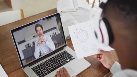 African-american-businessman-sitting-at-desk-using-laptop-having-video-call-with-male-colleague