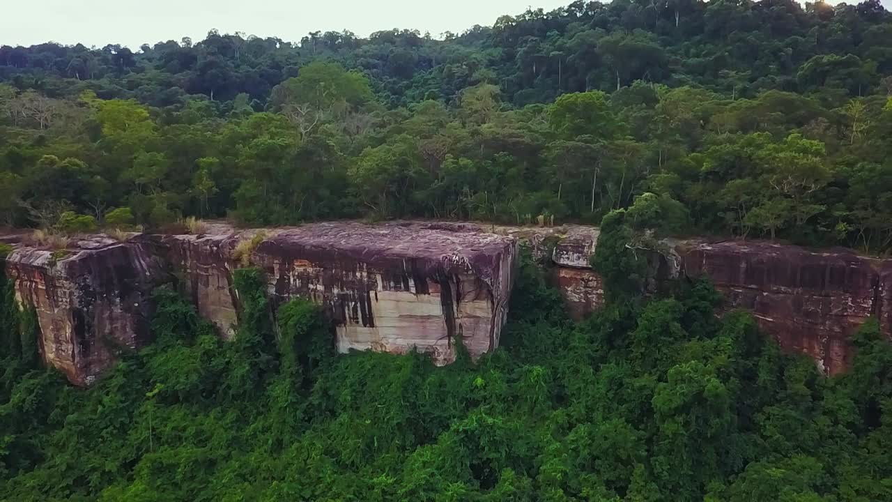 A group of tourists sitting on a cliff ledge in Phnom Kulen National Park near Siem Reap, Cambodia. Aerial pull back