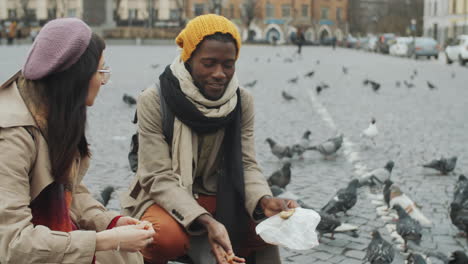 una alegre pareja de turistas alimentando palomas en la calle