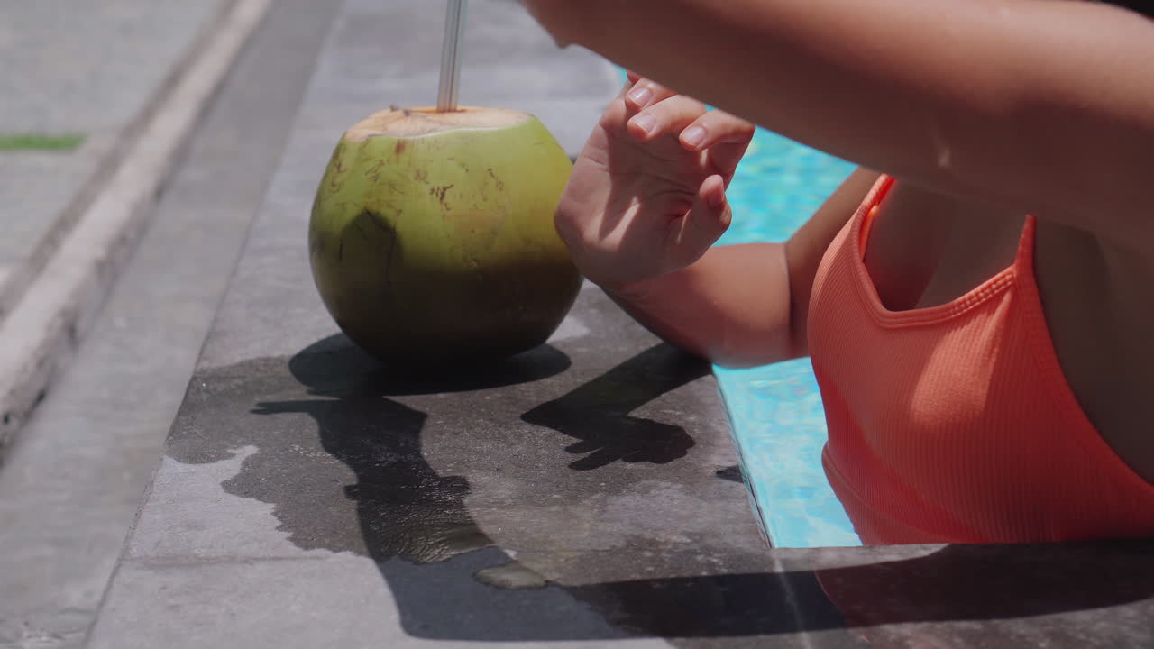 Woman relaxing by the pool with a coconut drink and smartwatch