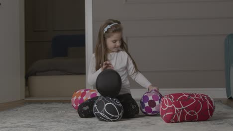 young girl trying to stack round cushions on floor before they fall over