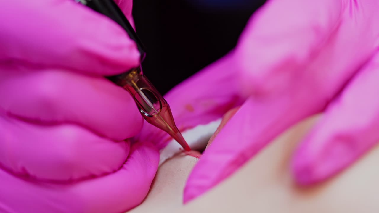 Applying red permanent makeup tattoo on lips. Tattooist in pink gloves making permanent make up on lips in beauty salon. Close-up.