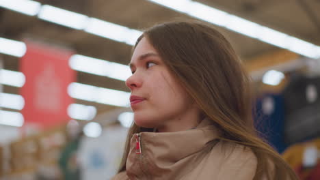 close-up of a young girl in a brown jacket, looking around in a mall. the background is blurred, emphasizing her curious and observant expression