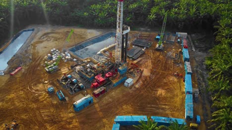 cinematic 4k drone footage of onshore drilling rig equipment structure for oil exploration and exploitation in the middle of jungle surrounded by palm oil trees during sunset and high oil price